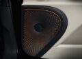 Close-up of a car door speaker with a black and orange perforated cover featuring a concentric circular pattern, labeled Bang & Olufsen—highlighting exclusive Bentley Mulliner interior options.
