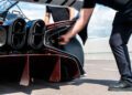 Two people stand near the rear of an exclusive Bugatti Bolide, with one person reaching toward the exhaust area, showcasing its impressive aerodynamic features.