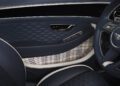 Close-up of a luxury Bentley car interior featuring blue leather, plaid fabric panel, chrome accents, and the Mulliner logo on the steering wheel—showcasing bespoke interior options.