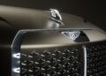 Close-up of a luxury EV Concept car’s front grille, featuring illuminated Bentley logos on the hood and grille in a dimly lit setting.
