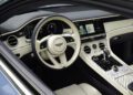 Interior view of a Bentley luxury car featuring a cream and black leather steering wheel, digital displays, Mulliner geometric patterned center console, and touchscreen navigation system with bespoke Interior Options.