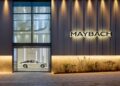 A silver Maybach car is displayed in a glass showroom at the world's first Maybach Brand Center in Seoul, with the Maybach logo illuminated on the building's exterior wall.