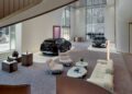 Modern showroom interior at the World’s First Maybach Brand Center in Seoul, featuring two cars on display, contemporary furniture, marble stairs, large windows, and minimalist decor.