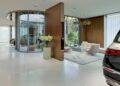 A modern, minimalist showroom in Seoul features luxury cars like Maybach, a glass-walled meeting room, and a seating area with white furniture and a vase of white flowers.