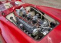 Close-up of a classic red sports car with the engine compartment open, revealing a detailed Ferrari 375 Plus engine and intricate mechanical components.