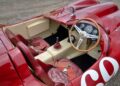 Close-up view of the interior of a vintage red Ferrari 375 Plus racing car, showing a wooden steering wheel, simple dashboard, leather seats, and gear stick.