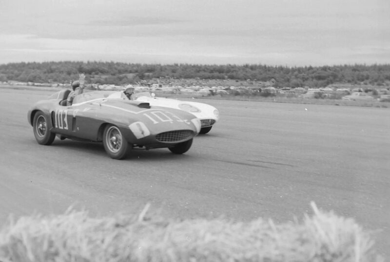 Two classic race cars, including a Shelby and car 104, compete on the racetrack with car 3 close behind under a cloudy sky, as spectators watch the intense battle for miles.