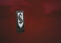 A close-up of a car emblem featuring a stylized "S" and the text "Sutton Hollywood Calif" on a glossy red surface, reminiscent of classic Shelby design details.