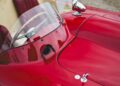 Close-up view of a vintage red convertible car's dashboard and steering wheel, reminiscent of a classic Ferrari 375 Plus, with tan and red interior and a small windshield—perfect for cruising miles of open road.