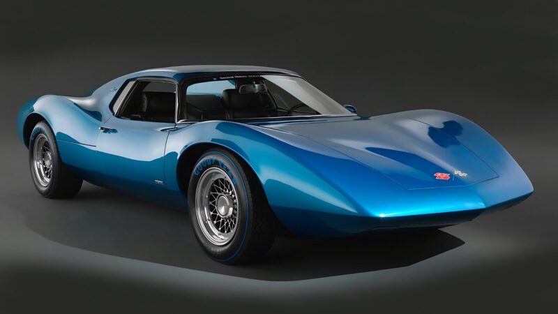 A sleek, blue vintage sports car with a low, aerodynamic body and wire-spoke wheels, photographed against a dark background—an example of the 10 Unsung Mid-Engine American Concepts That Pushed the Envelope Of Performance.