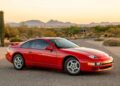 A red two-door sports car is parked on a paved road in a desert landscape with mountains visible in the background at sunset, evoking nostalgia for classic 90s cars for sale and the history they represent.