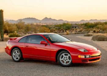 A red two-door sports car is parked on a paved road in a desert landscape with mountains visible in the background at sunset, evoking nostalgia for classic 90s cars for sale and the history they represent.