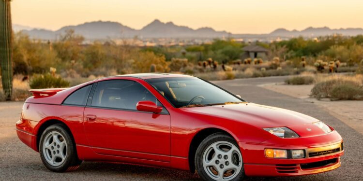 A red two-door sports car is parked on a paved road in a desert landscape with mountains visible in the background at sunset, evoking nostalgia for classic 90s cars for sale and the history they represent.