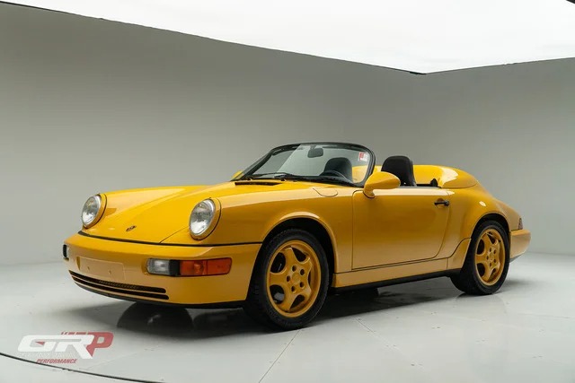 A yellow Porsche convertible sports car, radiating nostalgia, is parked in a white studio with its top down, viewed from the front left side.