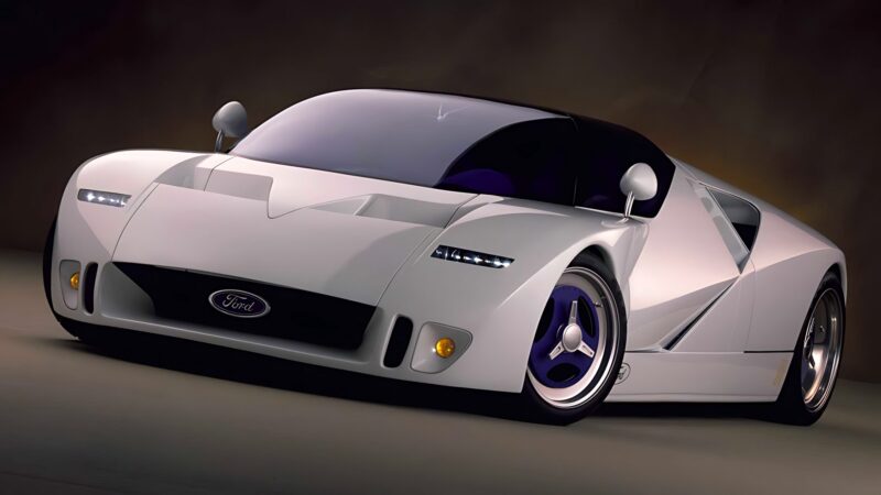 A white Ford concept sports car with a low, aerodynamic design, tinted windows, and distinctive blue-accented wheels stands out against a dark background—one of the 10 unsung mid-engine American concepts that pushed the envelope of performance.