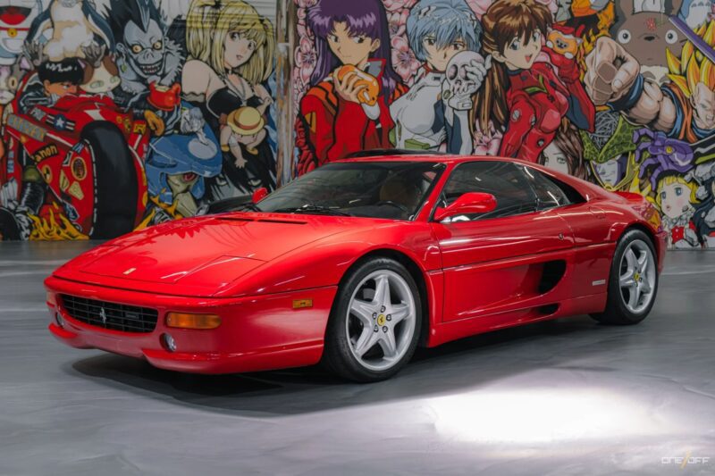 A red Ferrari sports car is parked indoors in front of a colorful mural featuring various anime characters, evoking nostalgia and celebrating the rich history of automotive thrills.