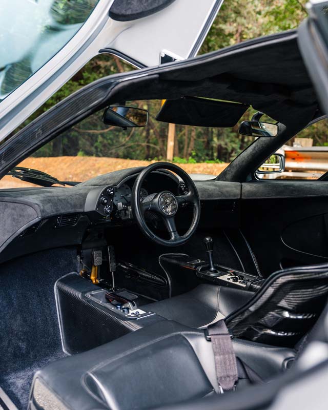 Interior view of a sports car at the Monterey Auction with the driver's door open, showing a black leather seat, steering wheel, and manual gear shift—an experience reminiscent of a McLaren F1 showcased by RM Sotheby's.