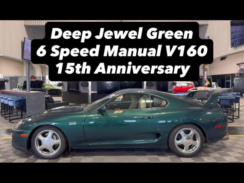 A dark green Toyota Supra sports car with a coupe body style is parked indoors, evoking nostalgia for 90s cars for sale. Text above reads: "Deep Jewel Green 6 Speed Manual V160 15th Anniversary.