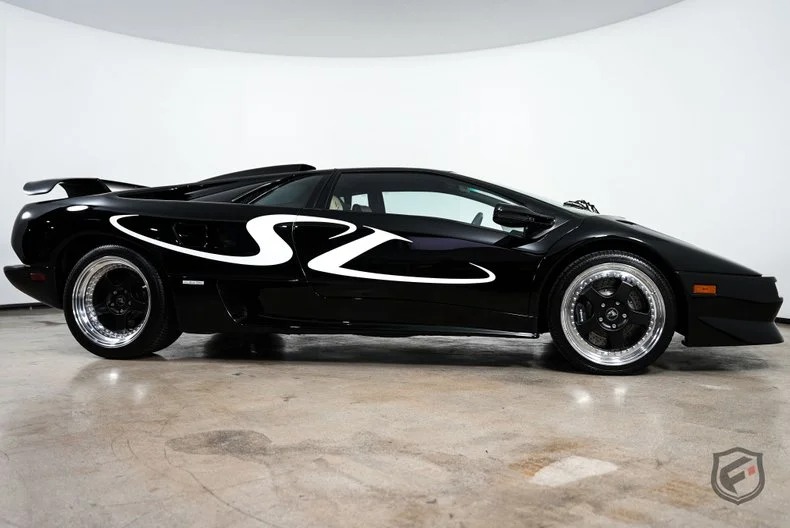 A black Lamborghini Diablo SV sports car with a distinctive white "SV" graphic on the side, photographed in a white indoor studio—an icon of 90s cars for sale that brings nostalgia and history to life.
