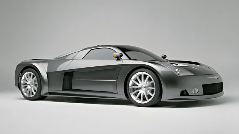 A sleek, silver sports car with aerodynamic design and large alloy wheels is parked in a studio setting, reminiscent of the 10 Unsung Mid-Engine American Concepts That Pushed the Envelope Of Performance.