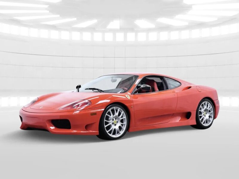 A red Ferrari luxury car is parked in a well-lit, modern white showroom with circular light fixtures on the ceiling.