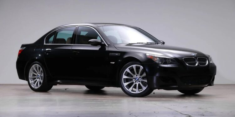 A black BMW sedan is parked indoors on a smooth concrete floor, viewed from the front left side against a plain light background—a striking example of stylish 2000s cars.