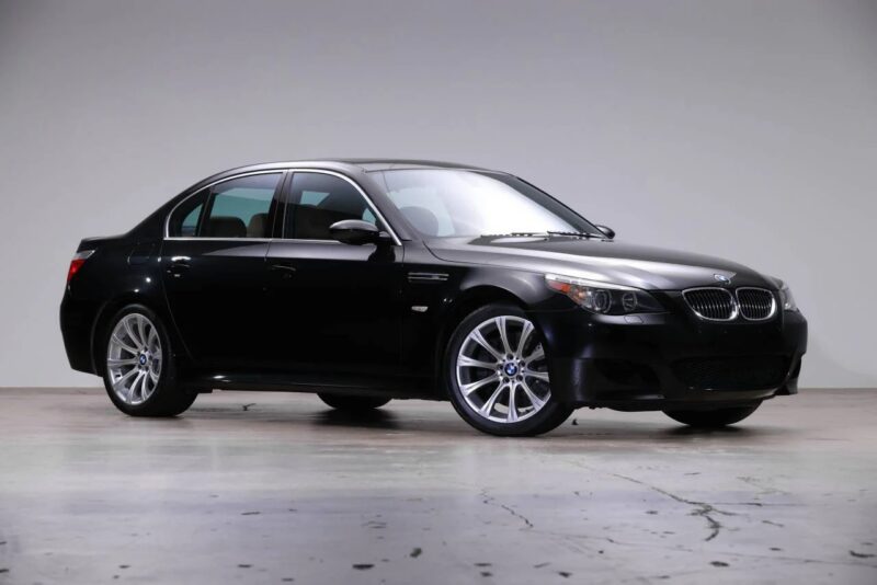 A black BMW sedan is parked indoors on a smooth concrete floor, viewed from the front left side against a plain light background—a striking example of stylish 2000s cars.
