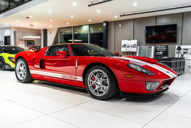 The Red Ford GT sports car with white racing lines, one of the best 2000s cars, parked inside on a white tile floor in a modern showroom.