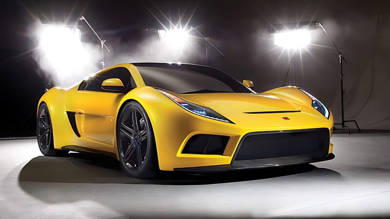 A yellow sports car, reminiscent of the 10 Unsung Mid-Engine American Concepts That Pushed the Envelope Of Performance, is parked in a studio with bright lights and mist in the background, highlighting its sleek and modern design.