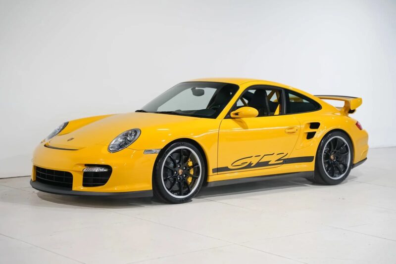 A yellow Porsche 911 GT2, one of the best 2000s cars, is parked indoors against a white background.