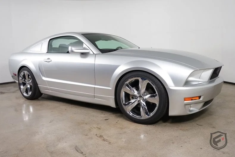 A silver Ford Mustang coupe, one of the best 2000s cars, parked indoors on a polished concrete floor and viewed from the front passenger side.