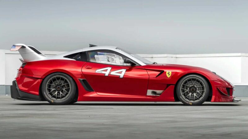 A red Ferrari 599XX EVO race car with the number 44 on the door, black wheels, and a large rear wing, parked on a concrete surface—set to turn heads at auction in Monterey.