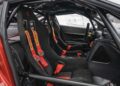 Interior of a Ferrari 599XX EVO race car featuring two black bucket seats with red Sabelt harnesses, a roll cage, and a stripped-down dashboard—set to go under the hammer at auction in Monterey.