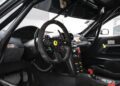 Interior view of a Ferrari 599XX EVO race car, featuring the iconic steering wheel with Ferrari logo, advanced control panels, and a racing seat with harness—soon to be available at auction in Monterey.
