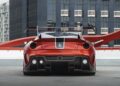 A striking Ferrari 599XX EVO with a large rear wing and black accents is parked in front of a modern glass building, capturing the excitement of Monterey auction week.