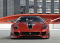 A red Ferrari 599XX EVO with black and white stripes is parked in front of a modern glass building with red details, ready to impress at the Monterey auction.