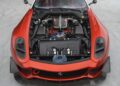 A red Ferrari 599XX EVO sports car with its hood open at auction in Monterey, showcasing a detailed view of the V12 engine and internal components.