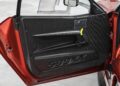 Close-up of a Ferrari 599XX EVO car door interior with a minimalist black panel, a yellow pull strap, and "599XX" embossed at the bottom—captured ahead of its Monterey auction.