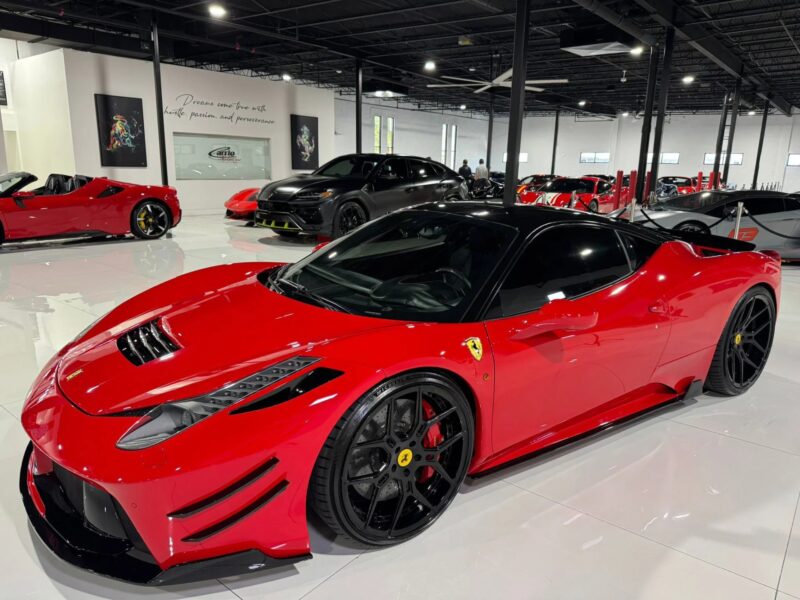 A red Ferrari 458 with black accents is parked in a showroom alongside other luxury vehicles under bright lighting, showcasing one of the best Ferrari 458 models for sale.