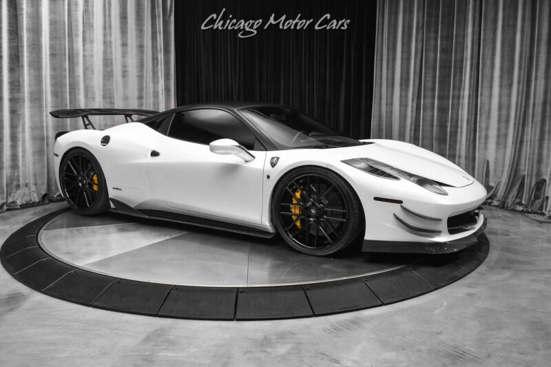 A white Ferrari 458 sports car with black wheels and yellow brake calipers is displayed on a rotating platform at Chicago Motor Cars, showcasing one of the best Ferrari models among their cars for sale.