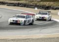 Two white BMW race cars, numbers 56 and 55, closely follow each other around a curve on the racetrack as BMW unveils new excitement ahead of Monterey Car Week 2025.