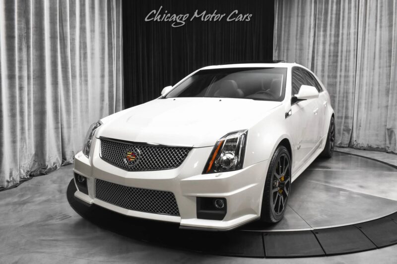 A white Cadillac CTS-V wagon, one of the best manual cars, is displayed on a turntable inside a showroom with "Chicago Motor Cars" written above.