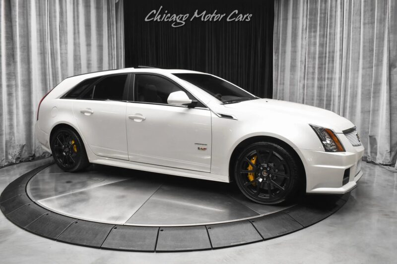 A white Cadillac CTS-V wagon with black wheels and yellow brake calipers is displayed on a turntable inside a showroom—an eye-catching example of luxury performance wagons.