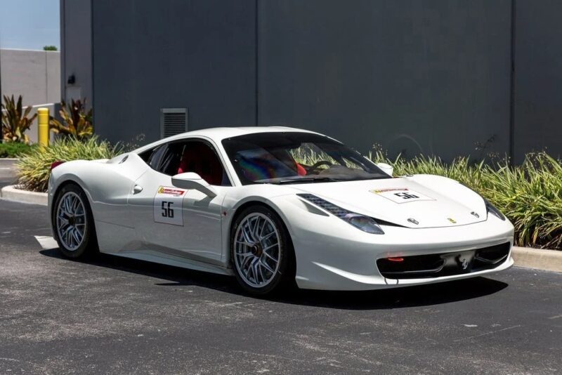 A stunning white Ferrari 458 sports car with racing number 56 is parked on a paved surface beside a landscaped area with bushes and grass, showcasing why it’s considered one of the best Ferrari 458 models around.