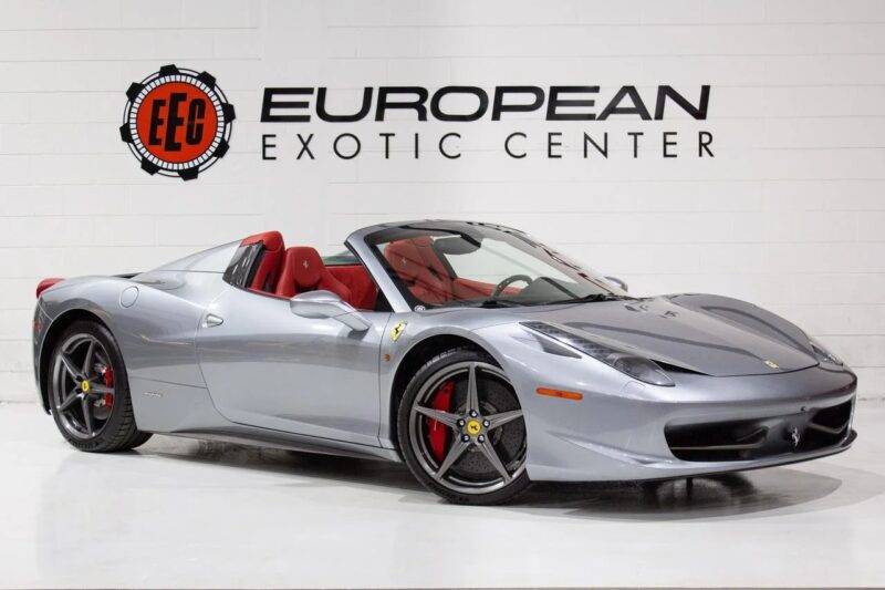 A silver Ferrari 458 convertible with red interior is parked indoors in front of a wall displaying the European Exotic Center logo, showcasing one of the best Ferrari cars for sale.