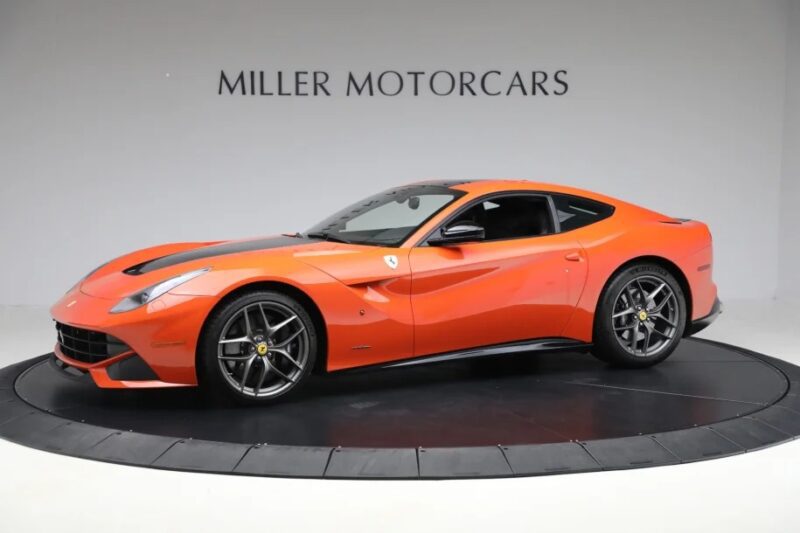 A red Ferrari F12 Berlinetta luxury car for sale is displayed in a showroom with "Miller Motorcars" written on the wall behind it.