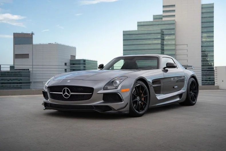 A silver Mercedes-Benz luxury car is parked on a rooftop with modern office buildings in the background.
