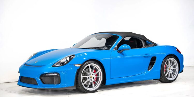 A high-performance Porsche convertible sports car with a black soft top is parked in a white studio setting, viewed from the side.