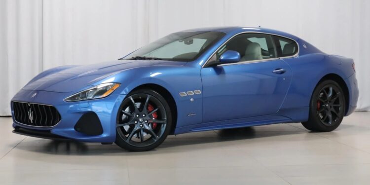 A blue two-door Maserati sports car with black wheels and red brake calipers is parked indoors against a white backdrop, showcasing Italian luxury.