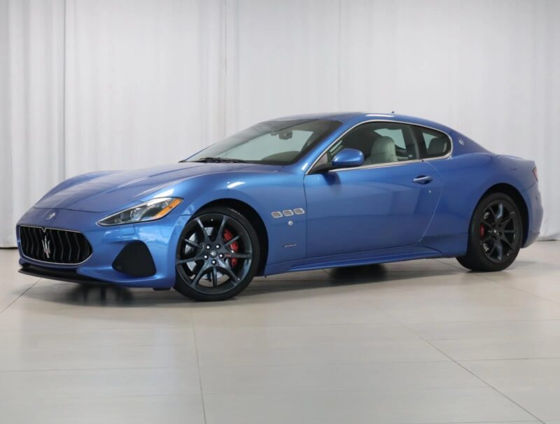 A blue two-door Maserati sports car with black wheels and red brake calipers is parked indoors against a white backdrop, showcasing Italian luxury.